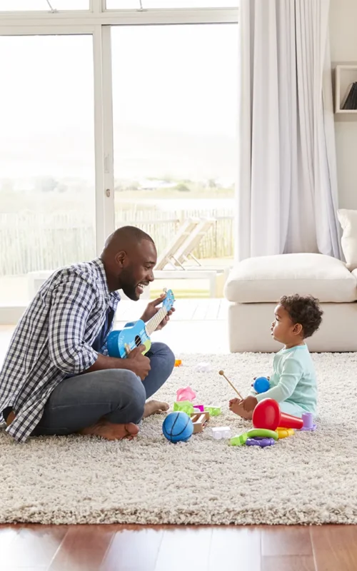 Homme jouant avec son enfant dans le salon sécurisé par une alarme pour maison